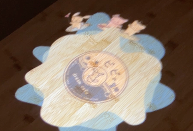 Projection mapping on a table featuring three cute characters surfing